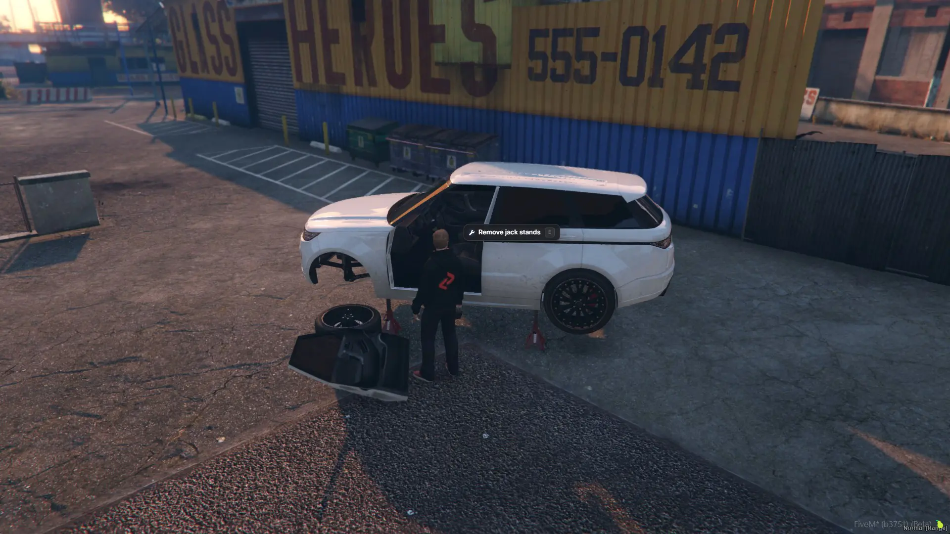 The driver's door on the ground beside the SUV, front wheel already gone, the car still up on its stands